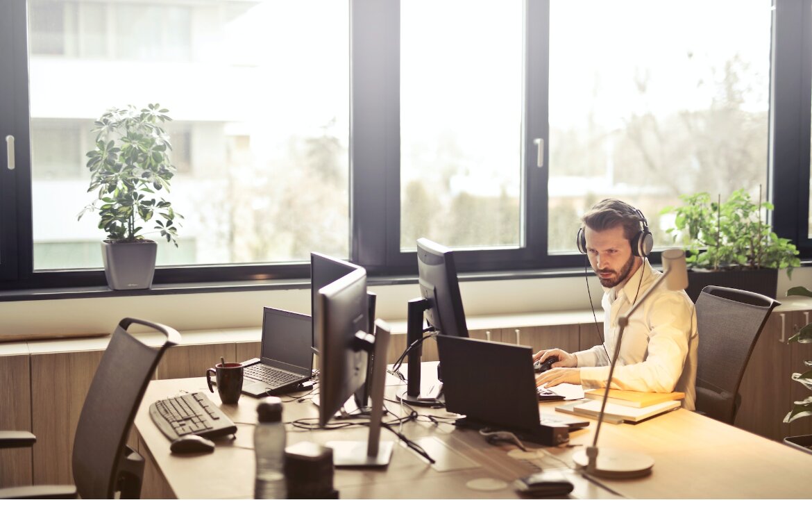 Junger Mann mit Headset sitzt in einem Büro vor einem Laptop.