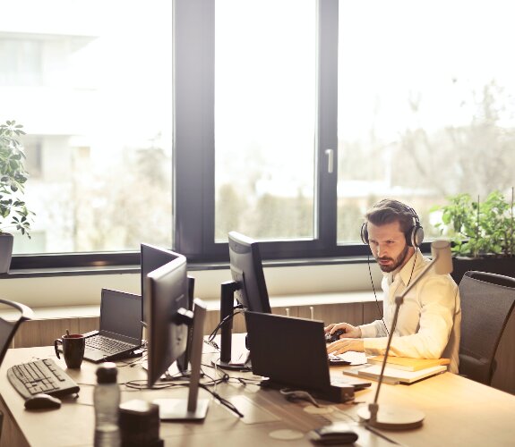 Junger Mann mit Headset sitzt in einem Büro vor einem Laptop.